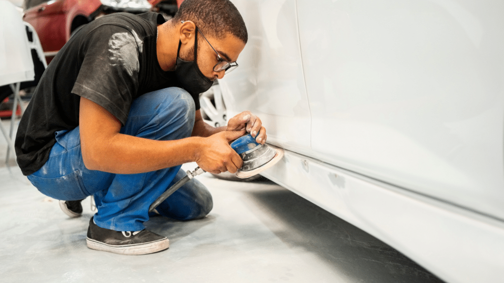 Mechanic sanding rocker panel of a car at workshop