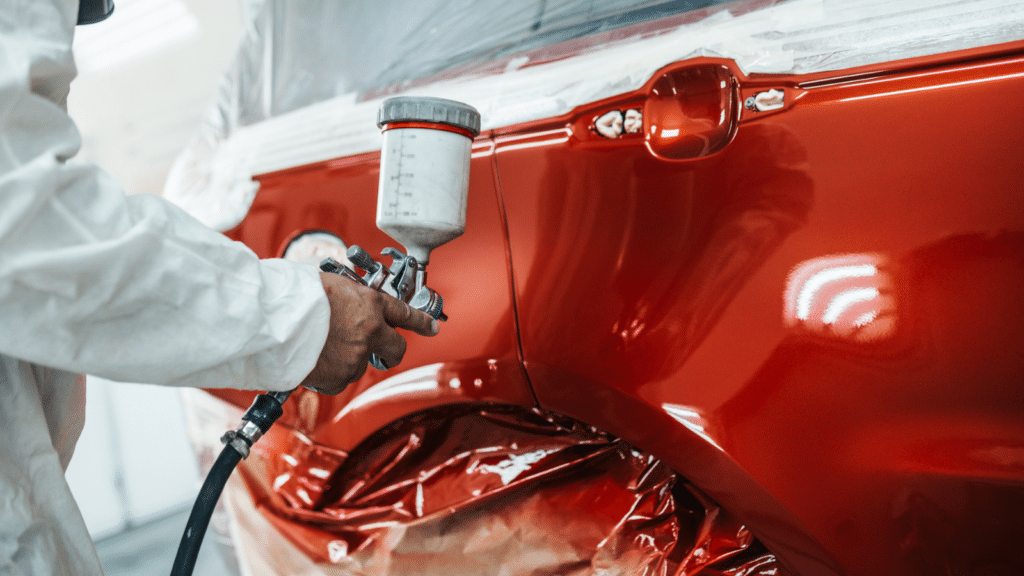 Man with protective clothes and mask painting car using spray compressor.
